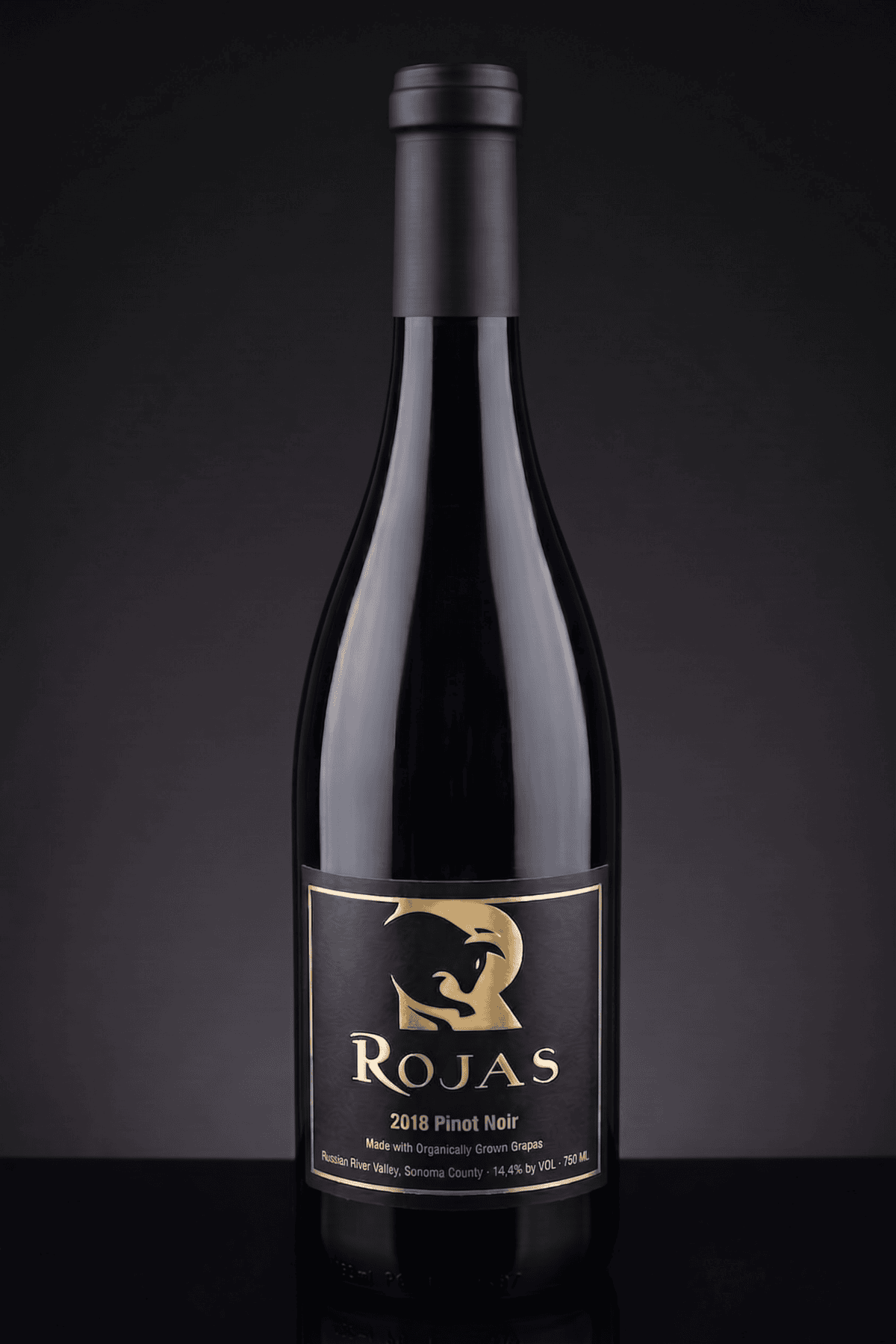 A bottle of Rojas 2018 Pinot Noir wine with a black and gold label featuring a stylized bulls head, set against a dark background.