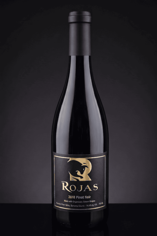 A bottle of Rojas 2018 Pinot Noir wine with a black and gold label featuring a stylized bulls head, set against a dark background.