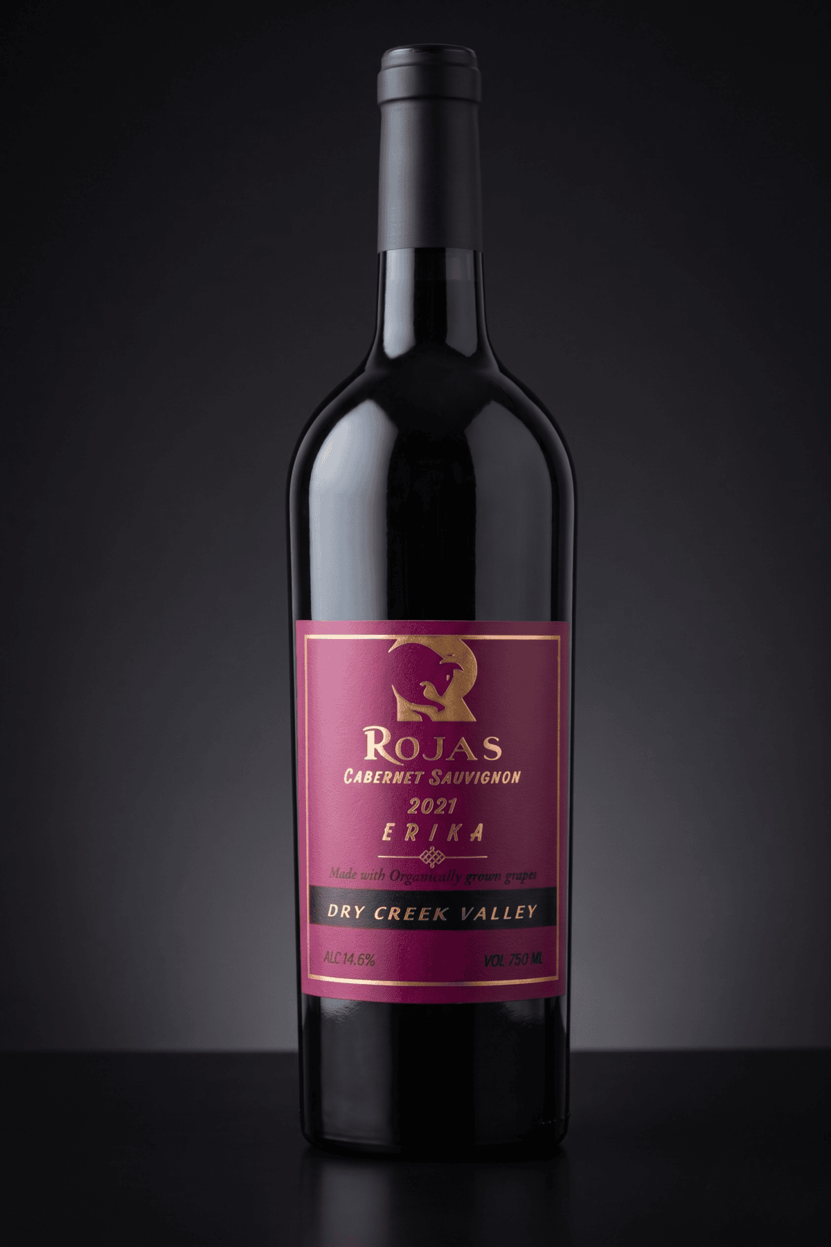 A bottle of Rojas Cabernet Sauvignon 2021 wine with a purple and gold label, set against a dark gradient background. The label highlights Dry Creek Valley and Made with organically grown grapes..