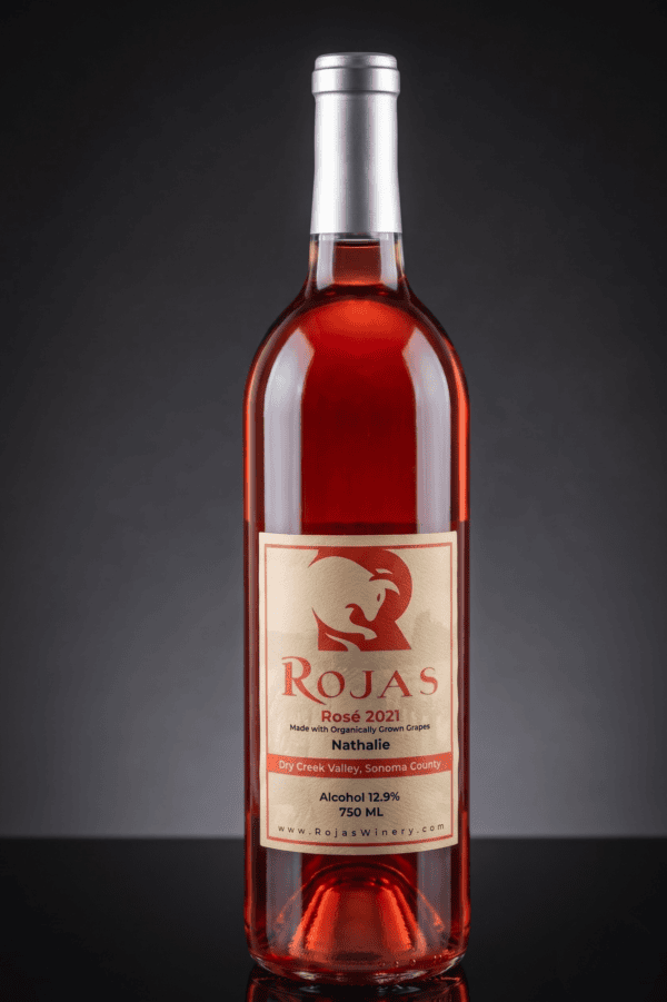 A bottle of Rojas Rosé 2021 wine with a metallic cap, filled with pink rosé, against a black background. The label lists Nathalie grapes and Dry Creek Valley, Sonoma County.