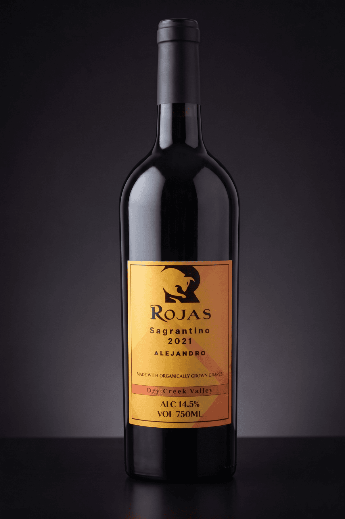 A bottle of Rojas Sagrantino 2021 red wine with a gold label, featuring Alejandro, Dry Creek Valley, 14.5% alcohol, and 750ml size, set against a dark background.