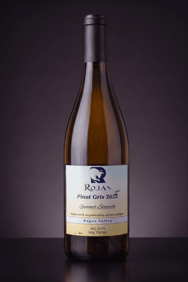 A bottle of Rojas Pinot Gris 2022 wine with a light cream label, featuring blue text and a bird logo, standing upright against a dark gradient background.