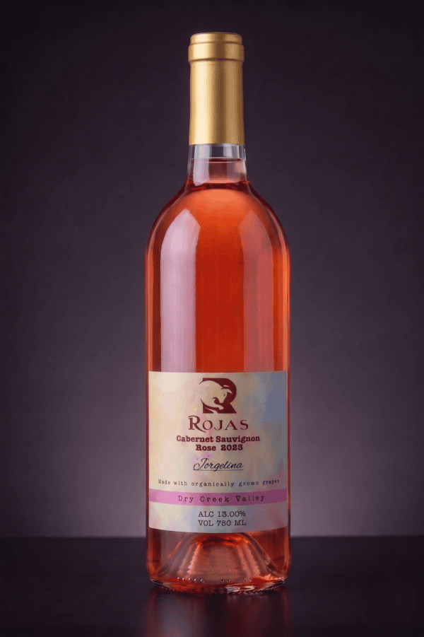A bottle of Rojas Cabernet Sauvignon Rosé 2023 with a gold cap, pink rosé wine, and a cream label, set against a dark gradient background.