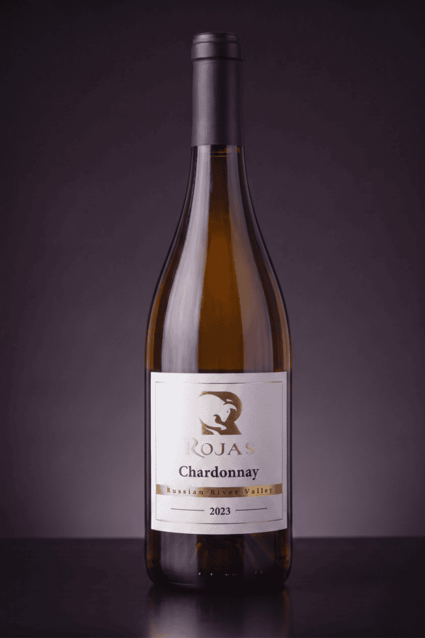 A bottle of Rojas Chardonnay wine from Russian River Valley, vintage 2023, stands upright against a dark purple background.
