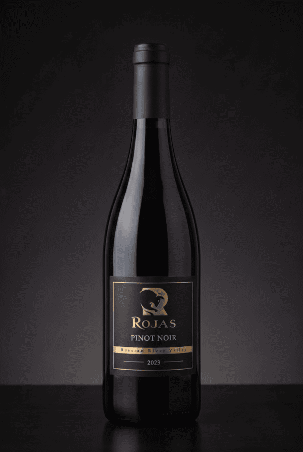 A bottle of Rojas Pinot Noir wine, vintage 2023, with a black and gold label, set against a dark, gradient background.