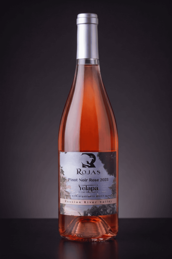 A bottle of Rojas Pinot Noir Rosé 2023 wine with a silver cap, pink liquid, and a label showing a black bird, trees, and text detailing its origin from the Russian River Valley.