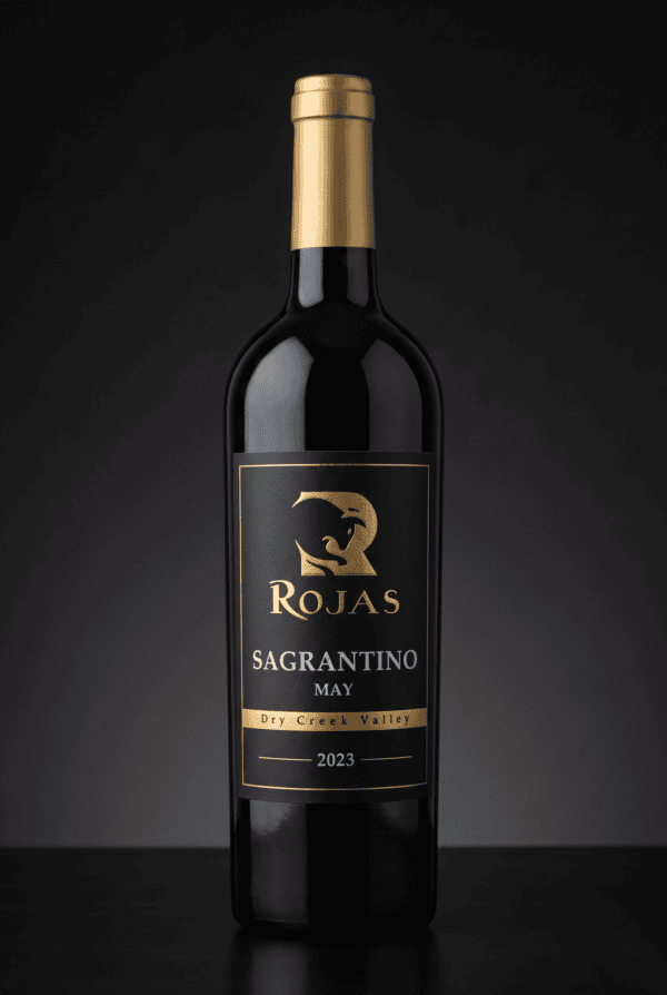 A bottle of Rojas Sagrantino wine, vintage 2023, with a gold label and cap. The label reads Dry Creek Valley and features a stylized animal logo. The background is dark and plain.