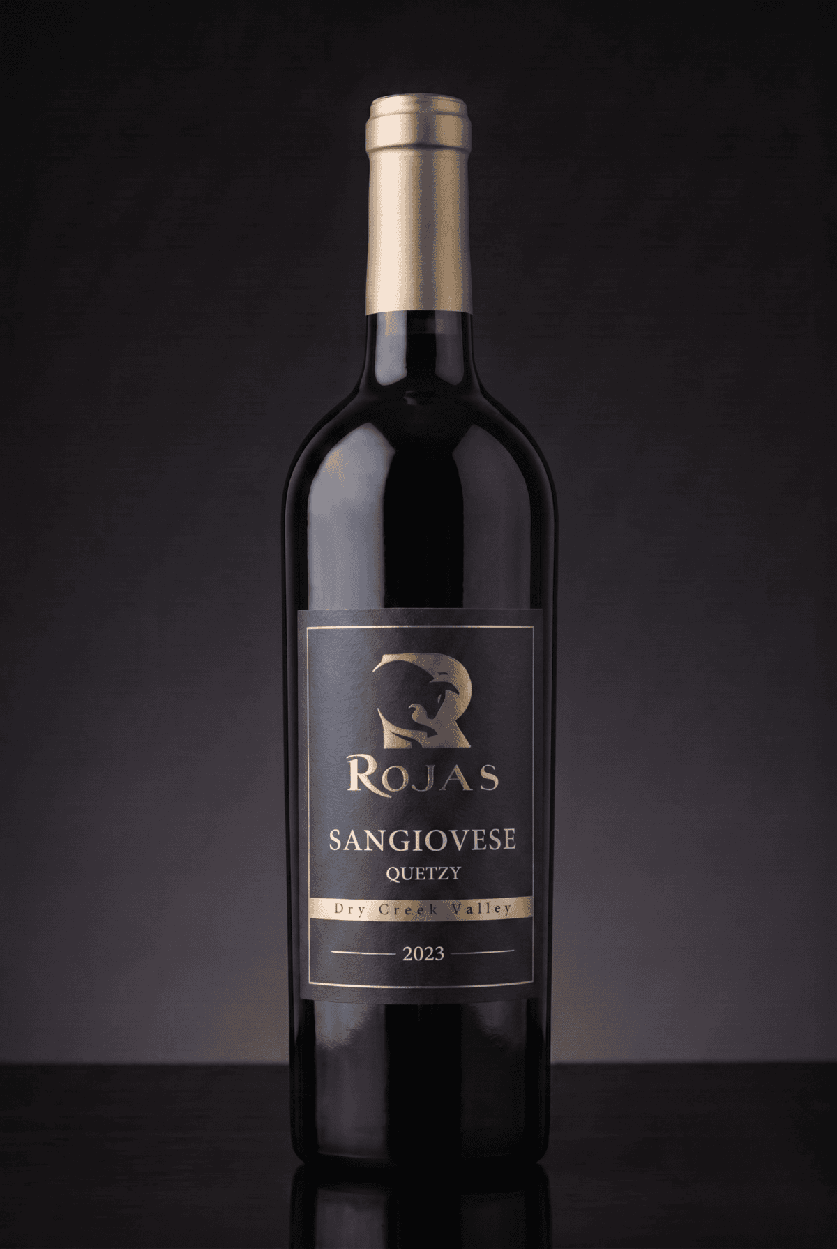 A dark glass wine bottle labeled Rojas Sangiovese Quetzy, Dry Creek Valley, 2023 stands upright against a dark gradient background.