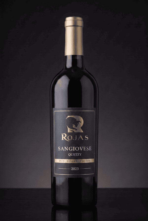 A dark glass wine bottle labeled Rojas Sangiovese Quetzy, Dry Creek Valley, 2023 stands upright against a dark gradient background.