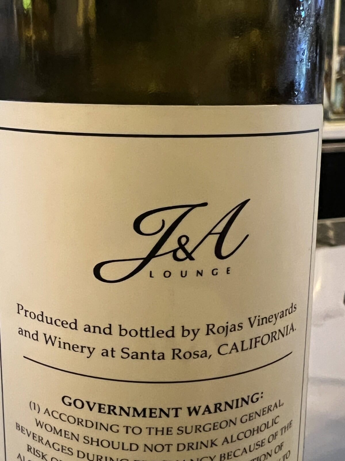 Close-up of a wine bottle label reading J&A Lounge, produced and bottled by Rojas Vineyards and Winery at Santa Rosa, California, with a partial government warning visible below.